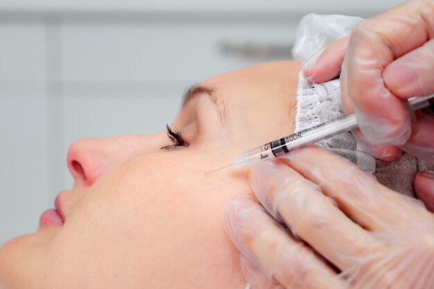 Beauty clinic employee injects filler to fill deep and small wrinkles on woman face CLOSE-UP