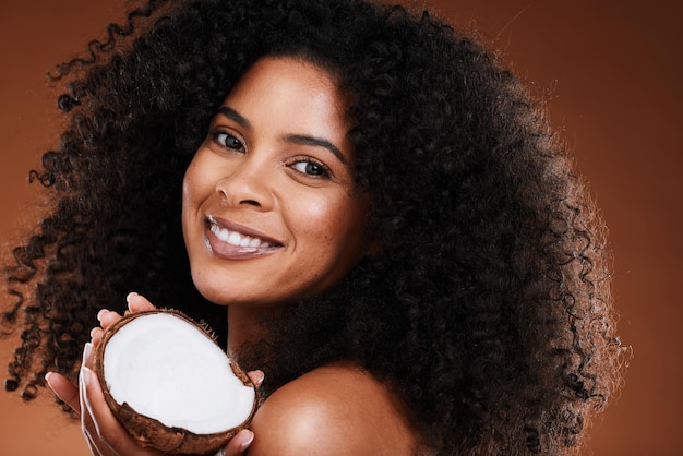 Beauty coconut and woman skincare or hair care with happy smile or curls for natural oil and brown studio background Portrait African American model and happiness with fruit and afro product