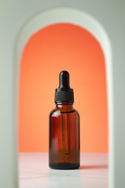 Beauty collagen face serum in a glass dropper bottle in Arch on orange background Trendy shoot of cosmetics packaging Essential oil with natural ingredients