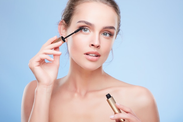 Beauty concept, head and shoulders of young woman with natural makeup. Girl looking up and painting lashes with mascara, applying mascara on eyelashes.