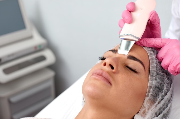 Beauty doctor with ultrasonic scraber doing procedure of ultrasonic cleaning of face Cosmetology and facial skin care