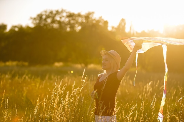 Beauty girl running with kite on the field. Beautiful young woman with flying colorful kite over clear blue sky. Free, freedom concept. Emotions, healthy lifestyle