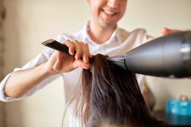 beauty, hairstyle, blow-dry and people concept -  close up of hairdresser with fan and brush making hot styling at hair salon