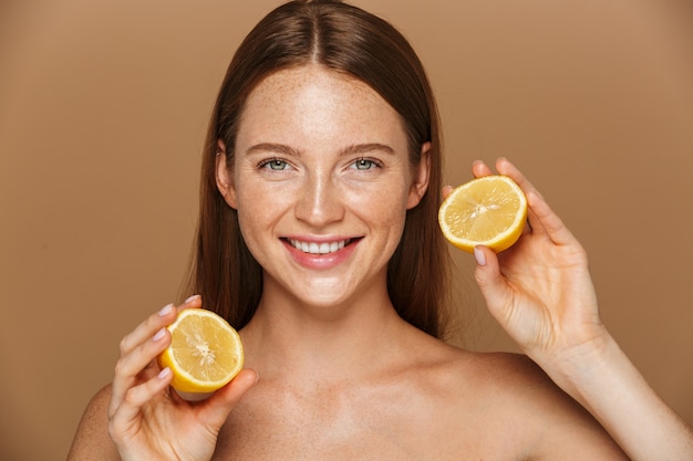 Beauty image of pretty shirtless woman with long hair holding two pieces of orange, isolated over beige background