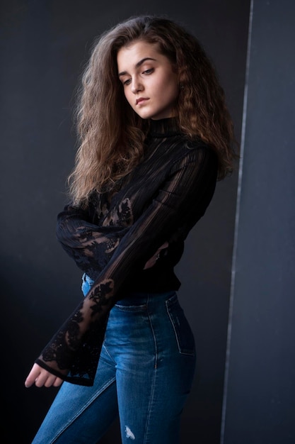 Beauty image of a pretty young woman with curly hair dressed in a black suitcase and jeans over grey background