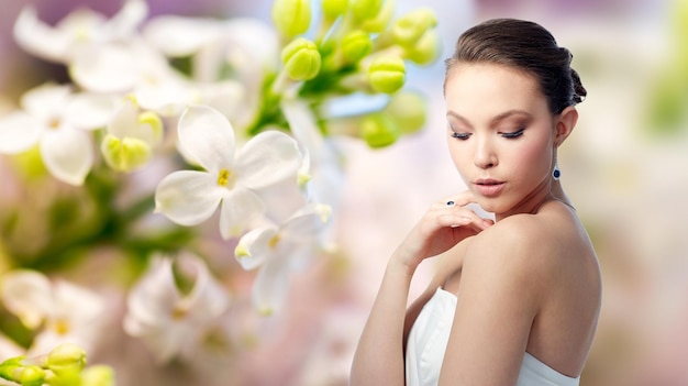 beauty, jewelry, people and luxury concept - beautiful asian woman or bride with earring and finger ring over natural spring lilac blossom background