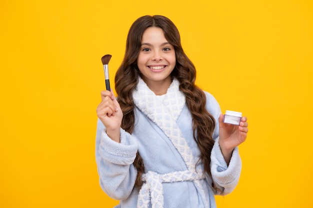 Beauty make up and kids cosmetics Teenage girl with brush applying blush to face isolated on yellow studio background