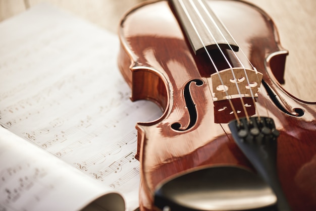 Beauty of musical instruments. Close up view of brown violin lying on sheets with music notes on wooden floor. Violin lessons. Musical instruments. Music equipment.