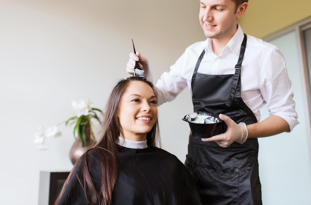 beauty and people concept - happy young woman with hairdresser coloring hair at salon