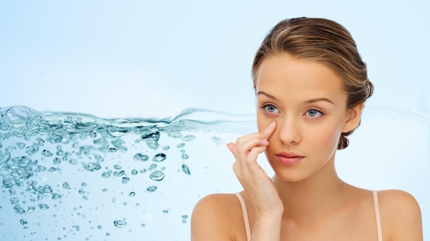 Photo beauty, people, cosmetics, moisturizing and skin care concept - young woman applying cream to her face over water splash background