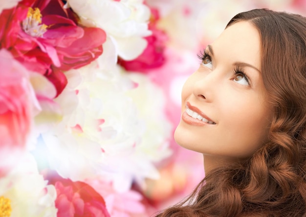 beauty, people and health concept - beautiful young woman looking up over pink floral background