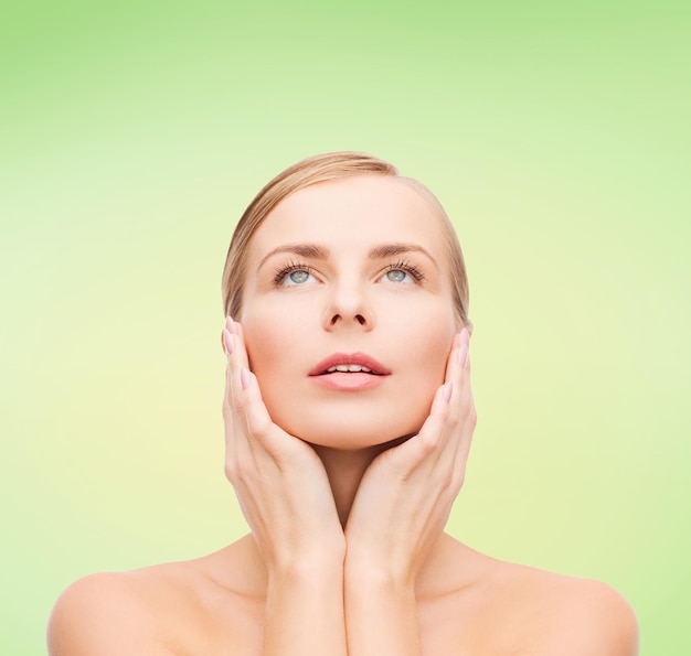 beauty, people and health concept - beautiful young woman touching her face over green background