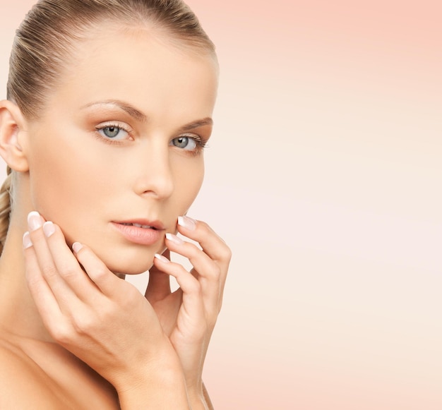 beauty, people and health concept - beautiful young woman touching her face over pink background