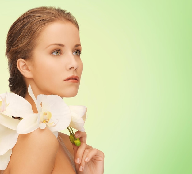 beauty, people and health concept - beautiful young woman with orchid flowers and bare shoulders over green background