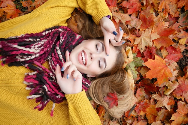 Beauty, people, season and health concept - pretty girl is lying in yellow red Autumn leaves