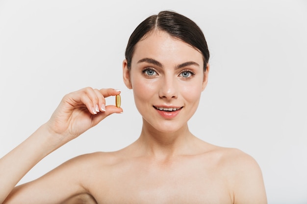 Beauty portrait of an attractive young topless woman isolated over white wall, taking beauty pills