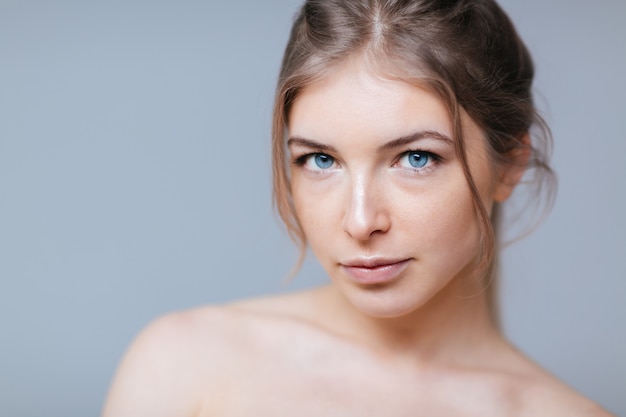 Beauty portrait of a charming woman with fresh skin looking at camera over gray background