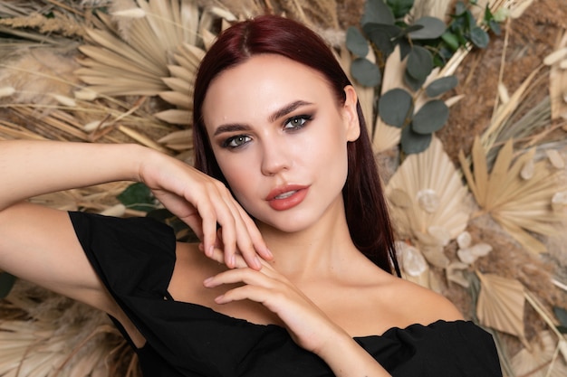 Beauty portrait of female face with natural skin. brunette girl with burgundy lips on a background of spring dry field flowers. open shoulders