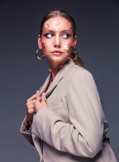 Beauty portrait of a girl Beautiful woman in a jacket posing with flower petals on her face on a gray background Femininity and beauty