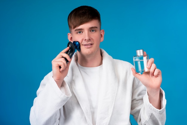 Beauty portrait of handsome guy, young attractive man shaving his face with electric razor shaver