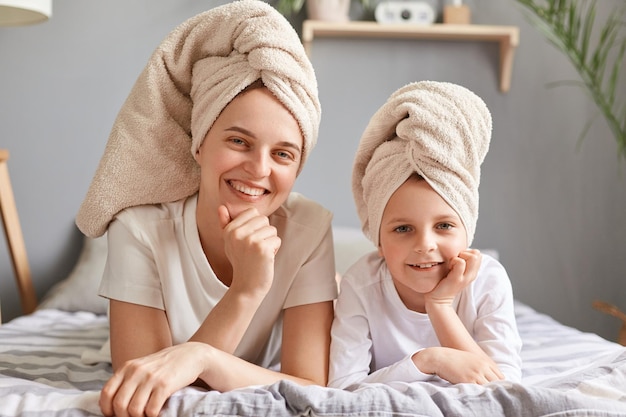 Beauty portrait of happy mom and daughter in towels on head lying on bed at home posing after bath having spa day cute little girl and her mother having fun together