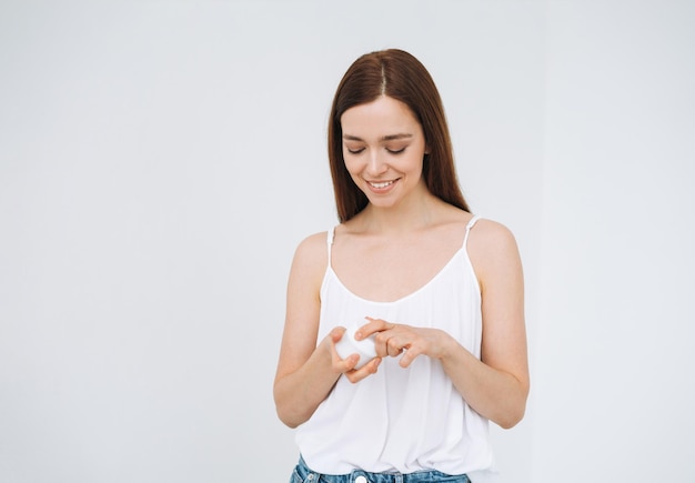 Beauty portrait of happy smiling woman with dark long hair put day nourishing moisturizer cream on clean fresh skin face and hands on the white background isolated