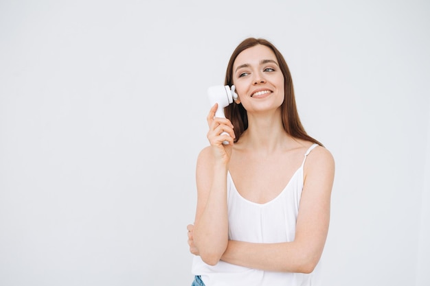 Beauty portrait of happy smiling woman with dark long hair with facial massager in hand on clean fresh skin face on white background isolated