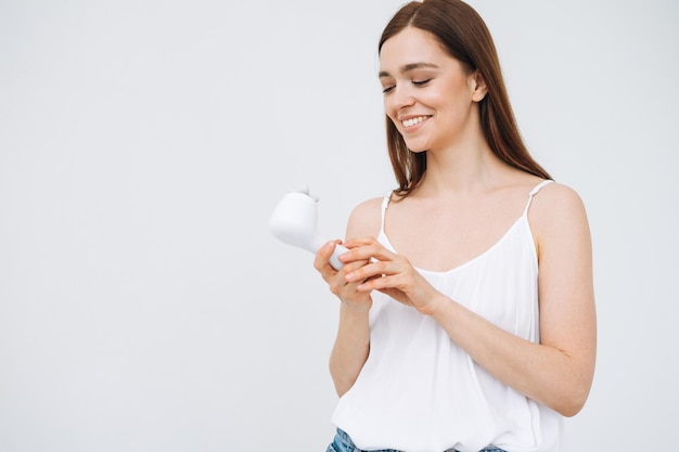 Beauty portrait of happy smiling woman with dark long hair with facial massager in hand on clean fresh skin face on white background isolated