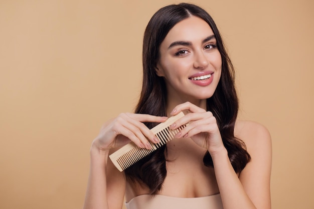 Beauty portrait of happy woman combing hair with wooden brush isolated on beige background