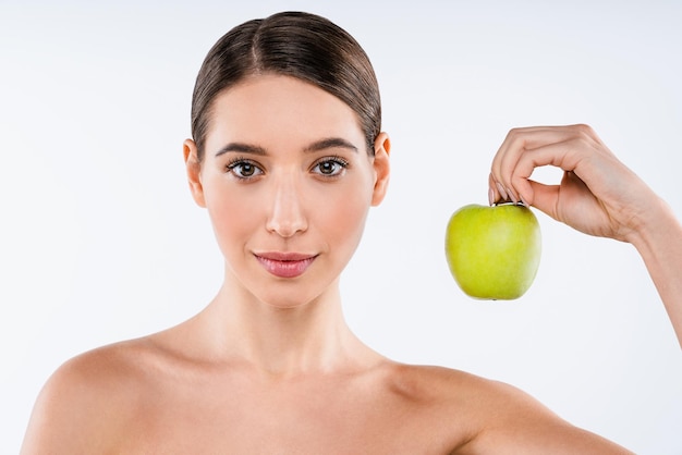 Beauty portrait of smiling young topless woman showing green apple while standing isolated