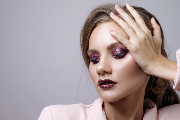 beauty portrait of woman on gray , fashion model in pink jacket with clean skin and beautiful lips, make up deep purple smokey eyes