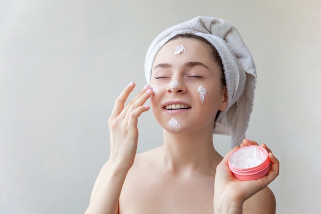 Beauty portrait of woman in towel on head with white nourishing mask or creme on face