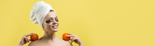 Beauty portrait of woman in white towel on head with gold nourishing mask on face Skincare cleansing eco organic cosmetic spa relax concept A girl stands with her back holding an orange mandarin