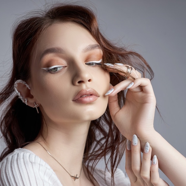 Beauty portrait of a woman with natural makeup and painted polished nails on her hand. Rings on the fingers of the hand