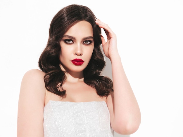 Beauty portrait of young brunette woman with evening makeup and perfect clean skin Sexy model with curly hair posing in studio With red bright natural lips In silver dress