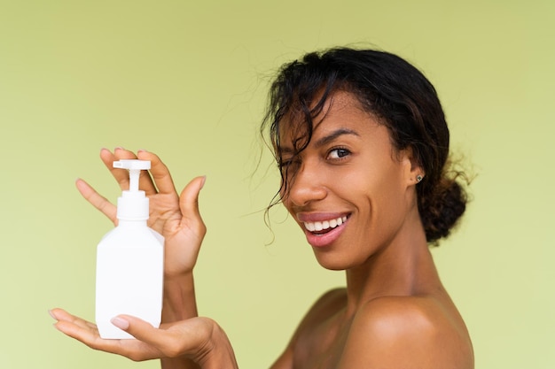 Beauty portrait of young topless african american woman with bare shoulders on green background with white bottle of body lotion