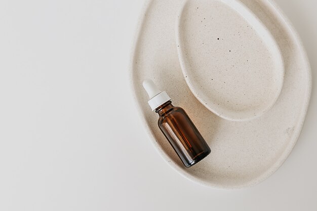 Beauty product glass bottle for serum, natural medicine , essential oil in ceramic plates  on a white background. Minimal, flat lay with copy space.