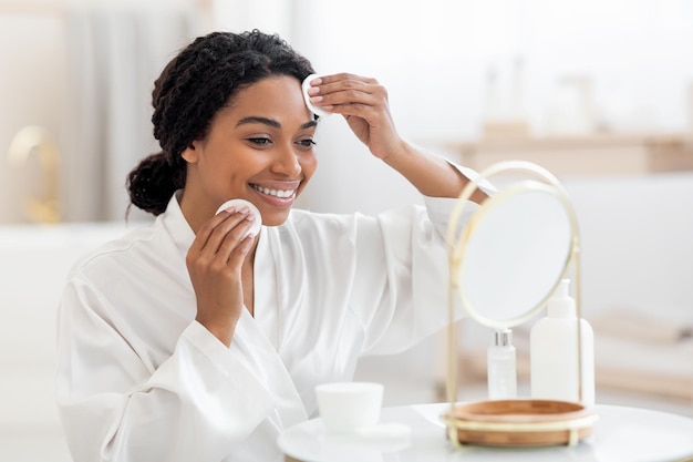 Beauty routine smiling black female looking in mirror and cleansing skin