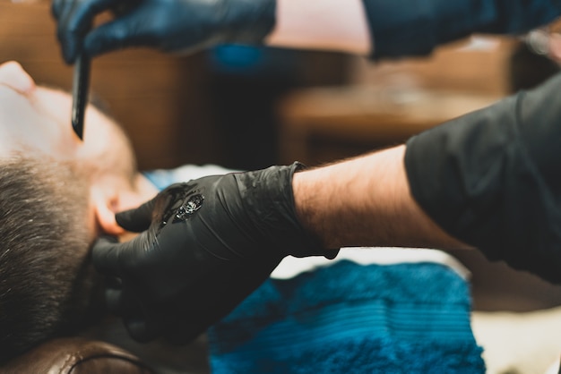 Beauty shop for men. Shaving a beard in a barbershop. Barber cuts his beard with a razor and clipper. close up Brutal haircuts. Hairdresser equipment. Selective focus.