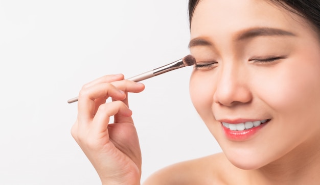 Beauty shot of smiley Asian woman with hand holding makeup powder brush on face. Cosmetic of perfect skin.