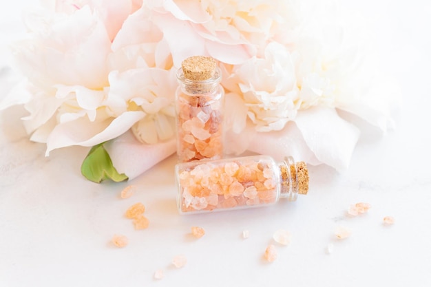 Beauty and spa concept Pink himalayan salt closeup in glass botles essential oil and peony flower in the background Selective focus