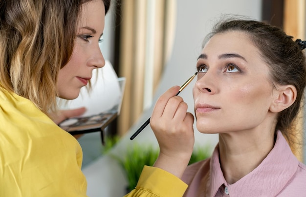 Beauty stylist applying makeup to a young model Professional Makeup artist doing glamour