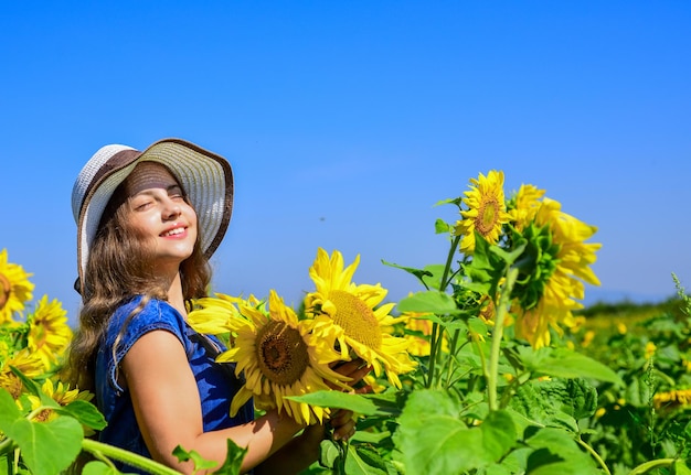 Beauty of summer nature little girl in sunflower field yellow flower of sunflower happy childhood beautiful girl wear straw summer hat in field pretty kid with flower Confidence in mind