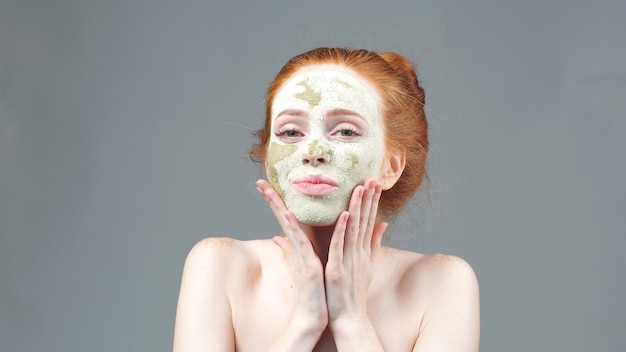 Beauty treatment. The girl applying a green clay mask for the face. aesthetic procedure