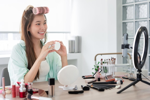 Beauty Vlogger concept Young woman showing jar of moisturizer cream to introduce product on Vlog