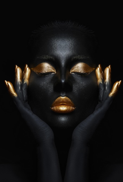 Beauty woman painted in black skin color body art gold makeup lips eyelids fingertips nails in gold color paint Professional gold makeup