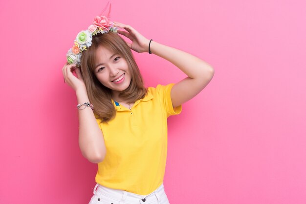 Beauty woman posing with flower hat in front of pink wall background