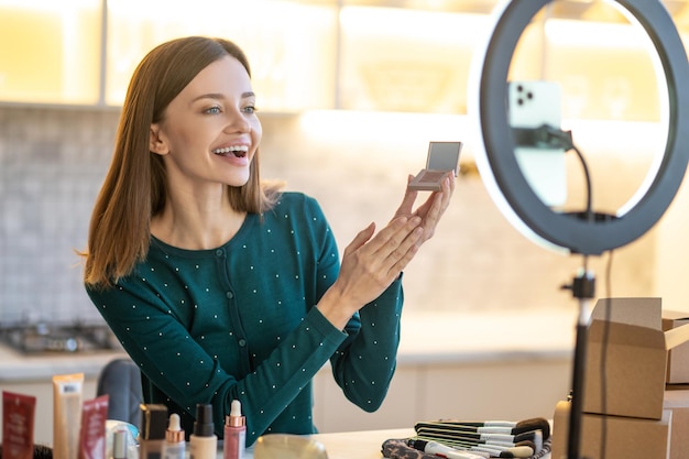 Beauty workshop. Young smiling woman shpowing new eyeshadows to onine audience