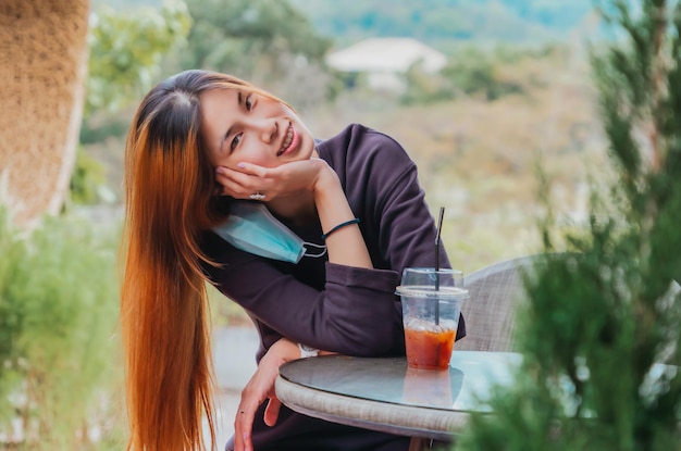 Beauty Young Asian smiling female is sitting in Cafe with forest nature background with Iced coffee on the table