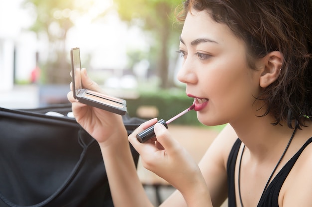 beautyful lady use lipstick to make up her face with mirror